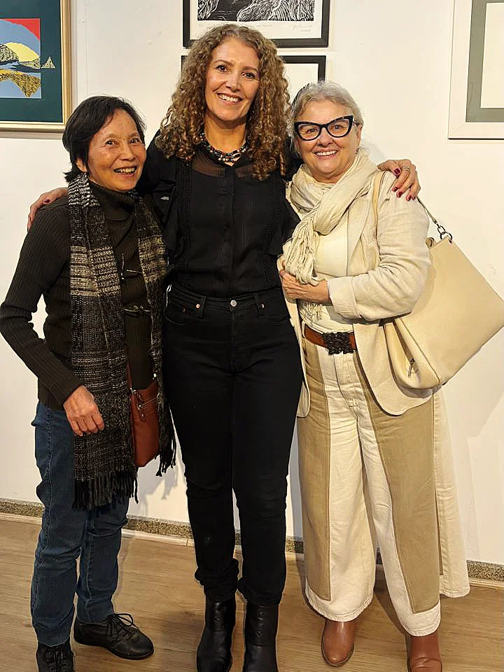Foto de três artistas mulheres em frente a uma parede com algumas obras